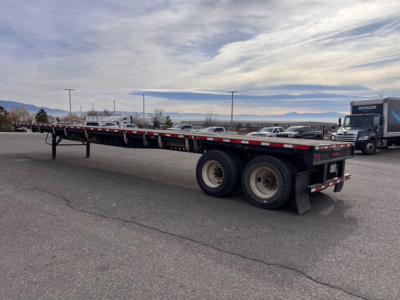 Flatbed trailer with tandem axles and slider steel flatbed showing side rails and rear lights.