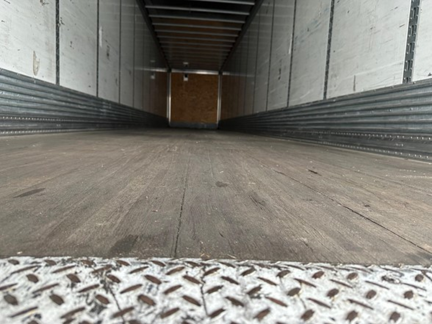 Trailer interior showing cargo space with wooden floor and metal side walls; front wall visible at far end.