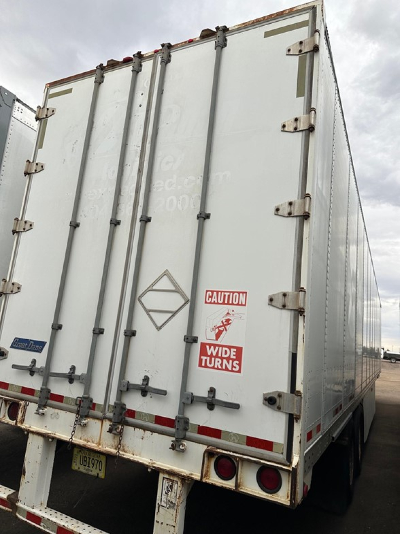 Rear view of a white trailer with multiple hinges and latches, CAUTION sticker, 'WIDE TURNS' sign, and Diamond logo on doors.