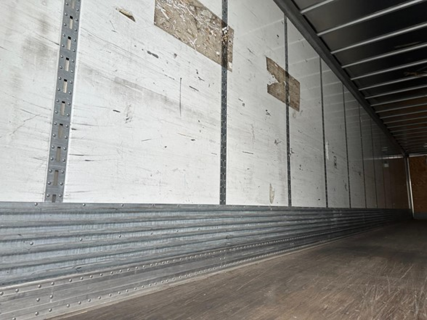 Truck trailer interior showing metal side walls and wooden floor with riveted aluminum trim.