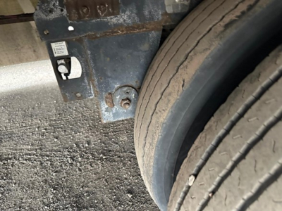 Van trailer frame with part of wheel and tire, showing metal bracket with a small label and a bolt.