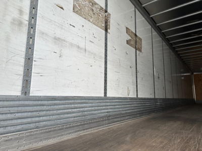 Trailer interior showing empty cargo space with ribbed metal walls and wooden floor, side rails and overhead ceiling.