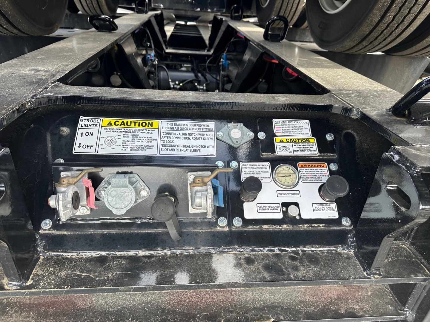 Trailer management panel with various valves and warning labels on Load King lowboy trailer showing control levers and gauges.