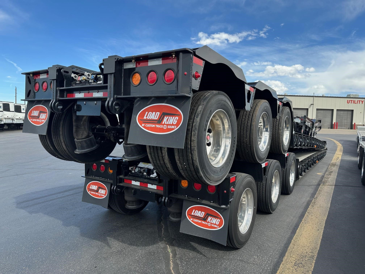 Load King lowboy trailer triple-axle with spare tires mounted, showing rear and side with Load King branding and red/white reflective tags.