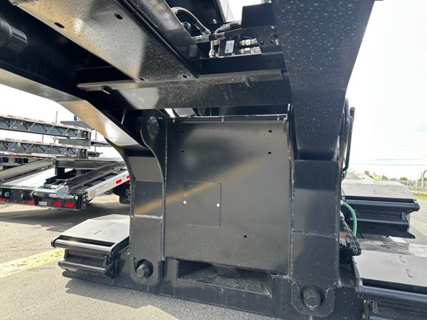 Lowboy trailer undercarriage showing black steel frame and mounting points with bolts and welded brackets.