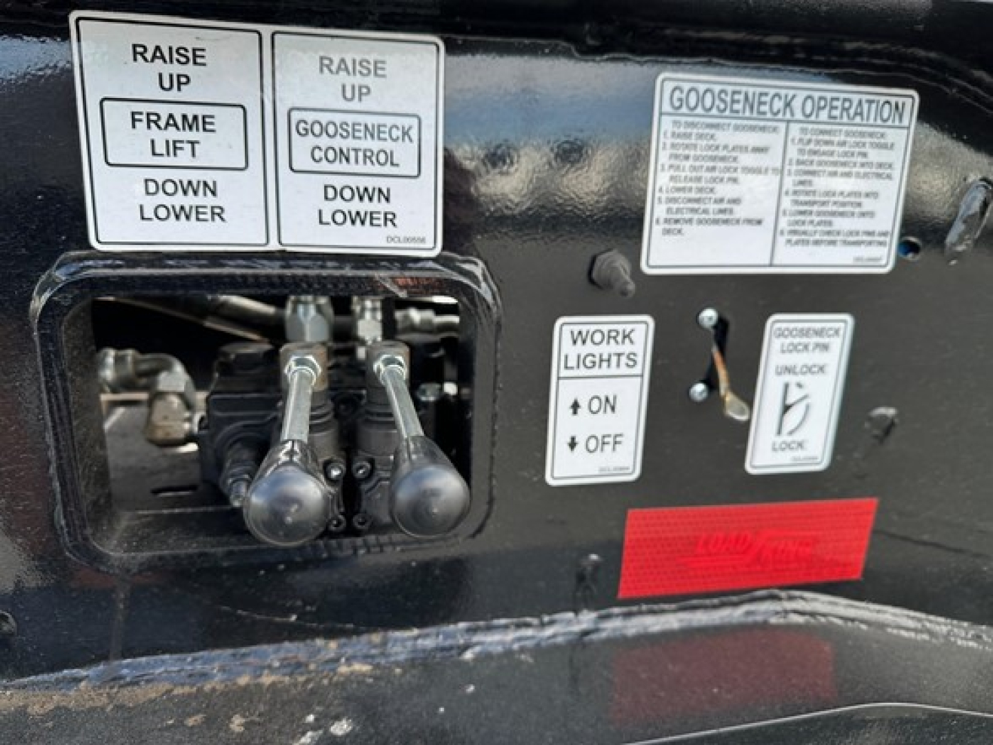 Control panel on Load King trailer showing raise up frame lift do down lower, gooseneck operation labels, work lights on off, and gooseneck lock/unlock switch with small red warning placard.