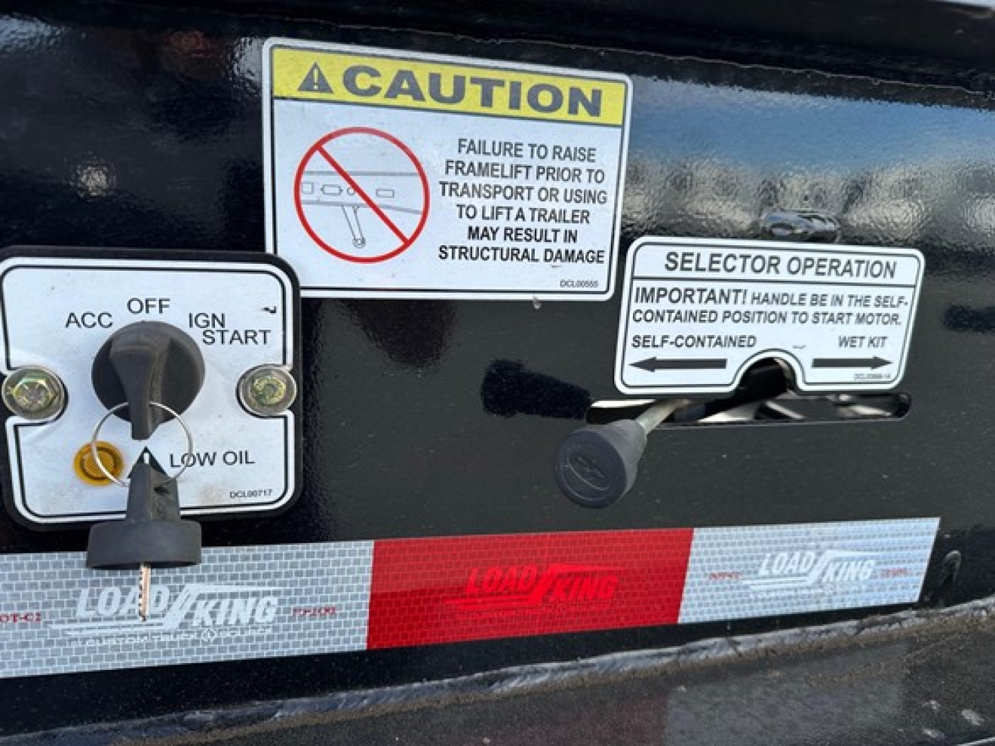 Trailer control panel with caution label and selector operation sticker; ignition OFF, engine start switch, low oil indicator; Load King branding on the frame.