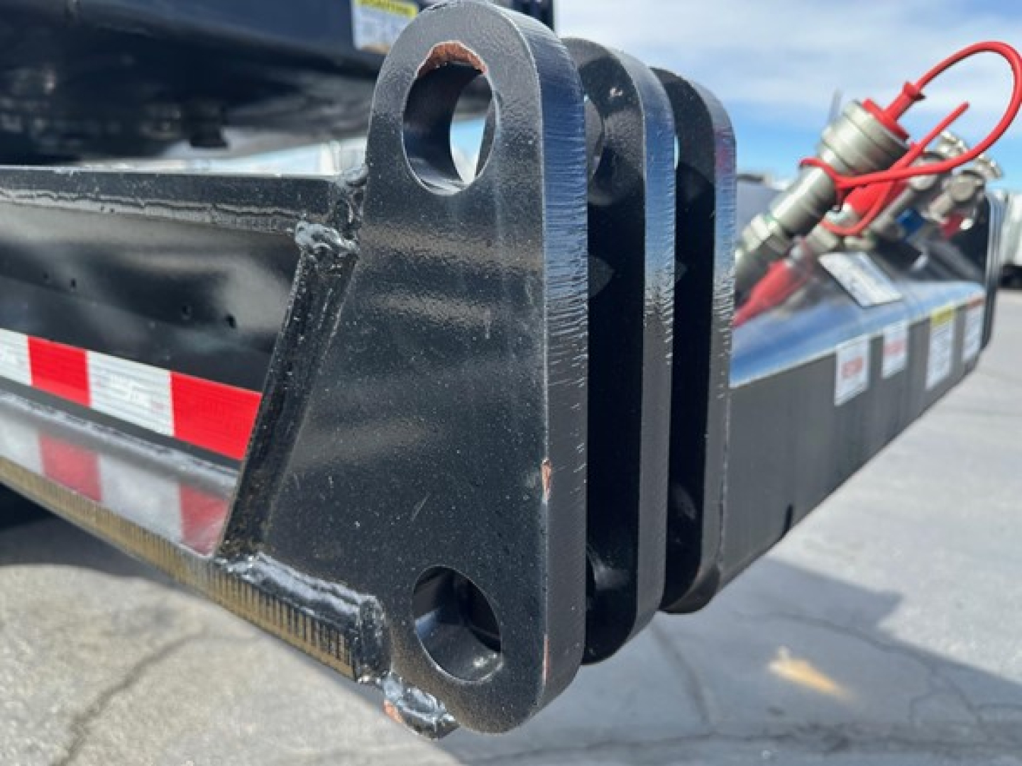 Load King trailer hitch and frame detail showing thick steel plate with rounded holes and welds, red hose/line in background.