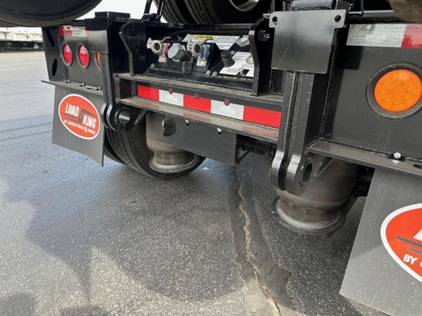 Rear view of a Load King lowboy trailer showing undercarriage components, red reflective strip, round reflectors, mud flaps with Load King logo, and suspension/axle area.