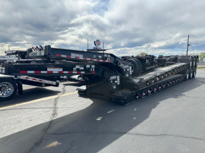 Lowboy trailer showing long flatbed deck and multiple axles, brand Load King 503/605 Ss Sff with black paint and reflective decals.