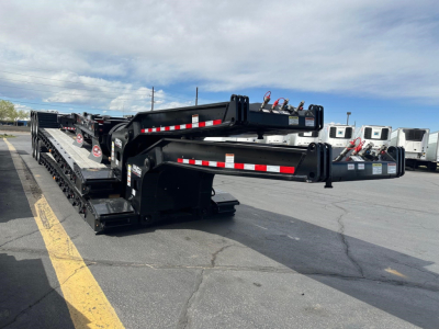 Lowboy trailer in a stacked storage pose showing heavy-duty gooseneck and ramps with reflective tape and hydraulic components.