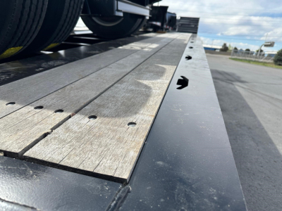 Load King trailer bed with wooden deck panels and metal edge rails, lowboy configuration, viewed from side near hitch area.