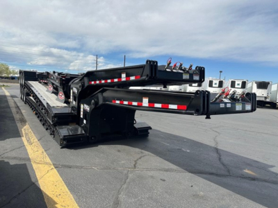 Lowboy trailer with multiple axles folded, black with red/white reflective strips, showing hitch area and frame details.