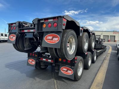 Load King lowboy trailer with triple-axle rear and spare wheels; visible text on mudflaps and back channels: LOAD KING logo, The Ultimate Heavy Haul, and trailer lights.