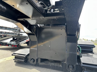 Lowboy trailer undercarriage showing black steel frame and mounting points with bolts and welded brackets.