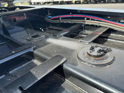 Trailer chassis showing top deck hardware and hydraulic lines with circular access port and metal brackets in a Load King trailer.