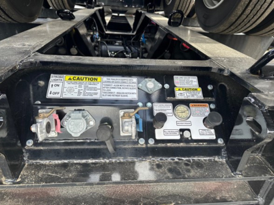 Trailer hitch area with control panel and warning labels on Load King lowboy trailer showing caution stickers, valve levers, and gauges.