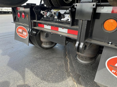 Rear view of a Load King lowboy trailer showing undercarriage components, red reflective strip, round reflectors, mud flaps with Load King logo, and suspension/axle area.