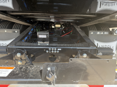Traveling axle trailer undercarriage showing frame rails, hydraulic lines, control box, and wiring; chrome hitch and inspection plate visible.