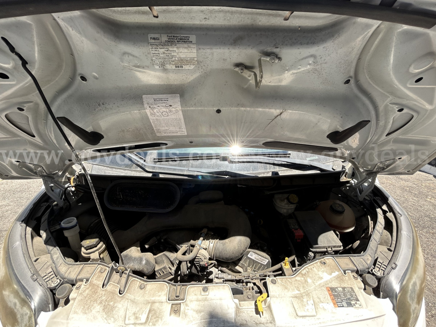 Ford Transit engine bay view with hood open showing engine components and labeled stickers.