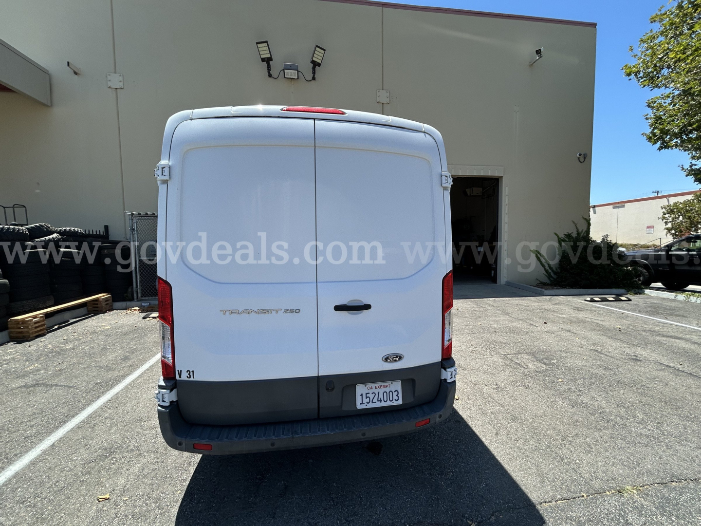 Ford Transit cargo van rear view in a parking lot with refrigerated category. Visible rear doors, Ford badge, taillights, license plate in lower right, stock number label, and VIN plate top left of rear doors.