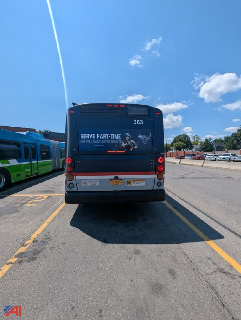 Bus rear view showing model number 383 and safety/advertising text; two taillights, license area, and rear bumper with warning decals; clear blue sky.