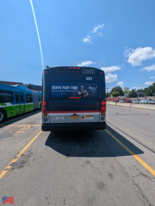 Bus rear view showing model number 383 and safety/advertising text; two taillights, license area, and rear bumper with warning decals; clear blue sky.