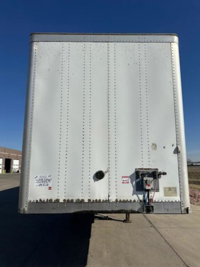 Rear view of a silver Wabash trailer with loading lights and bumper hitch, small circular vent, riveted panels, and warning stickers.