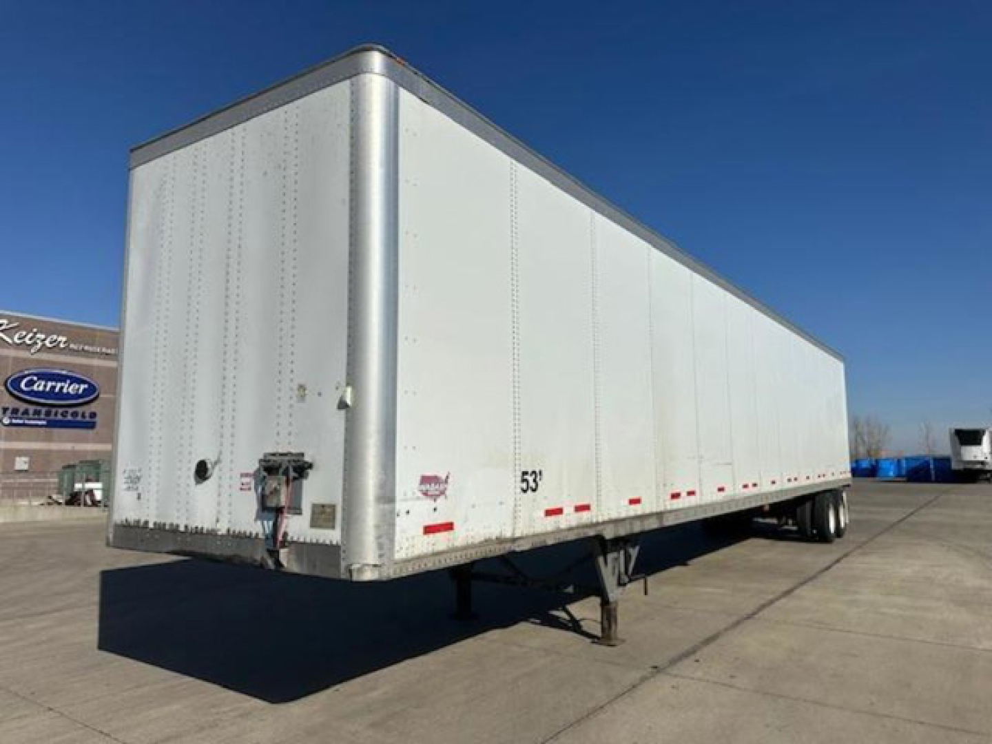 Trailer side view showing 53' dry van with white aluminum exterior, rear doors, and support legs visible.