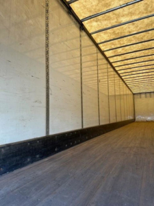 Interior of an empty Wabash dry van trailer with wooden floor, white side walls, and steel side posts; no visible text or markings inside.
