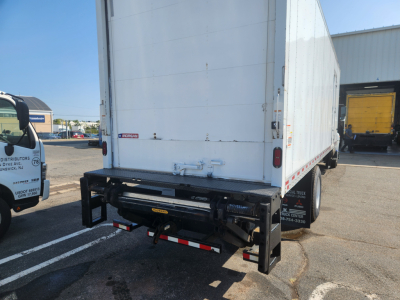 Rear view of a box truck trailer showing a black rear bumper/step with reflective tape and utility hooks under the cargo area; white box body with hinge and latch hardware.
