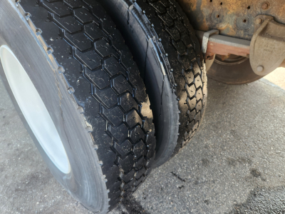 Truck wheel and dual tire setup showing tread pattern and inner wheel; part of chassis and undercarriage with some rust-colored components.