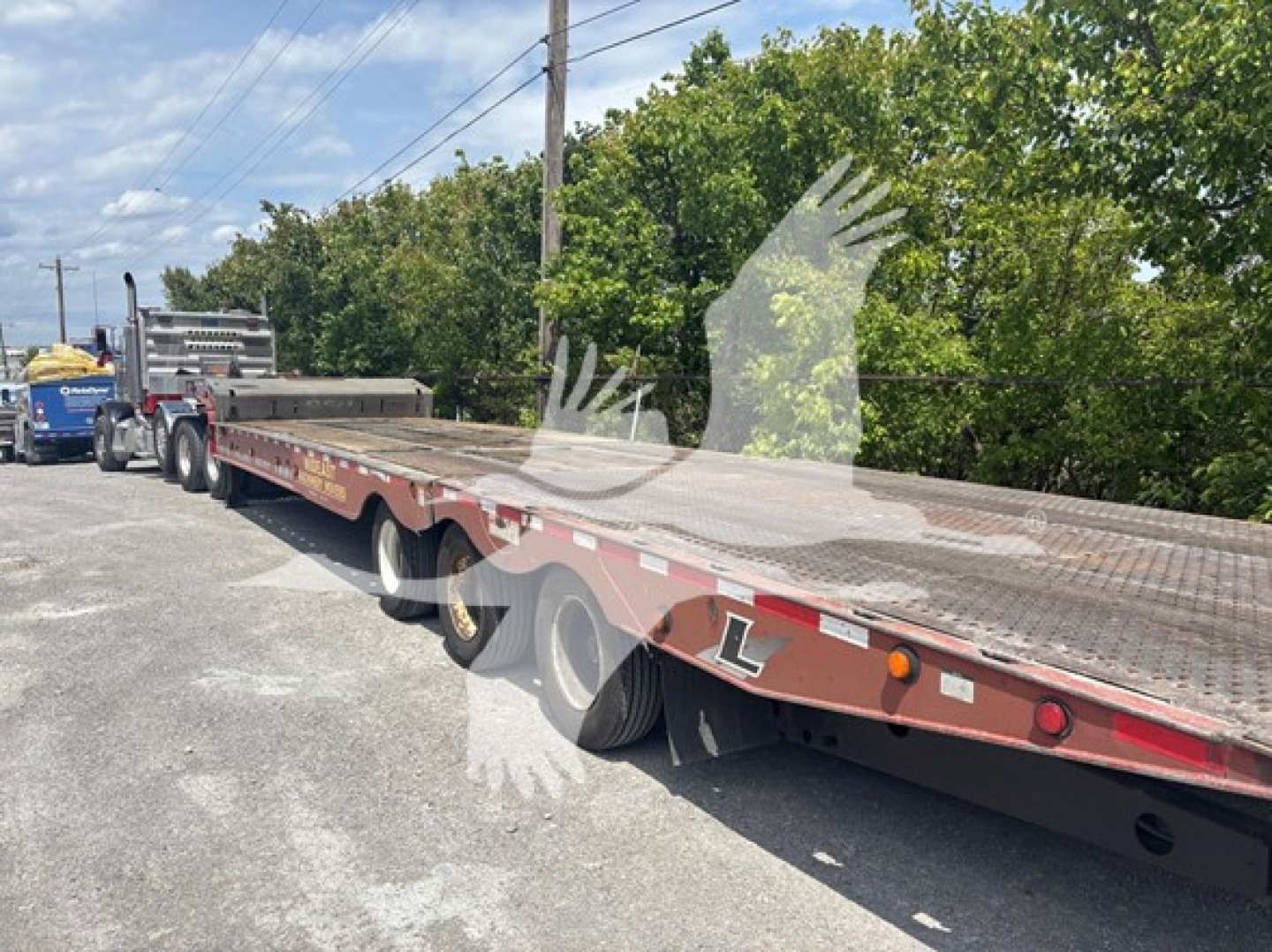 Trailer deck of a 2015 Landoll 950c traveling axle trailer with dual rear axles and long low-bed, visible VIN sticker area and stock tag; shows flatbed with red-brown paint and reflective markings.