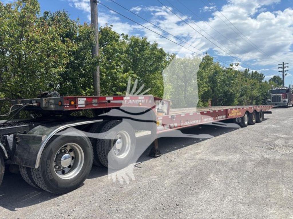 Long red Landoll 950C traveling axle trailer with multiple axles and tires, parked on gravel lot; side view showing trailer deck and wheelsets.