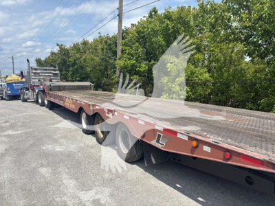 Trailer deck of a 2015 Landoll 950c traveling axle trailer with dual rear axles and long low-bed, visible VIN sticker area and stock tag; shows flatbed with red-brown paint and reflective markings.