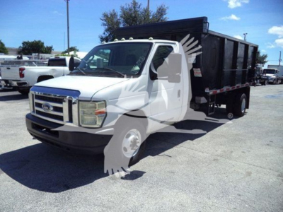 Ford E450 dump truck with white cab and black dump body, side view in a lot.