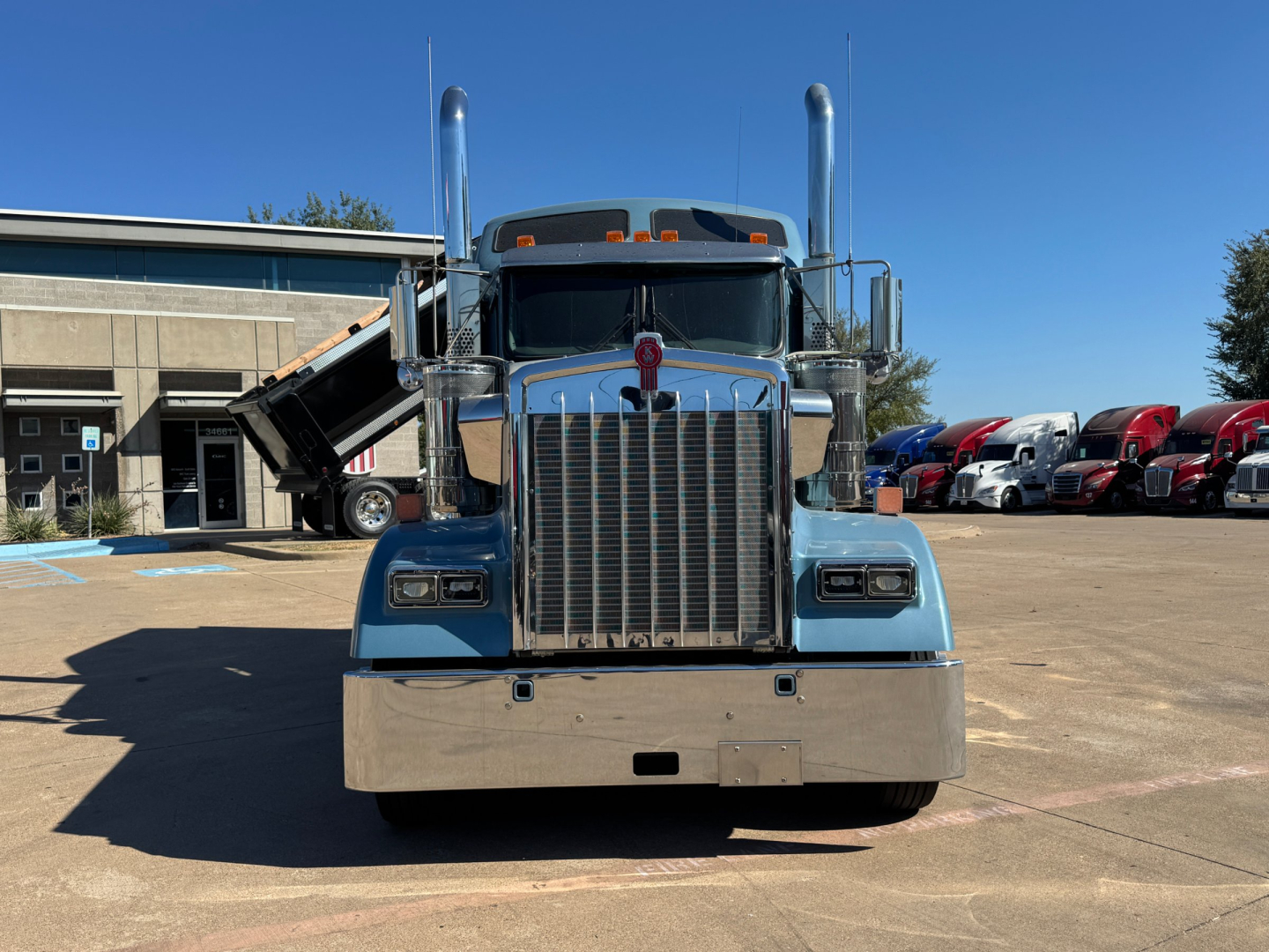 Front view of a blue 2025 Kenworth W900L conventional sleeper truck showing chrome grille, tall exhaust stacks, and large bumper.