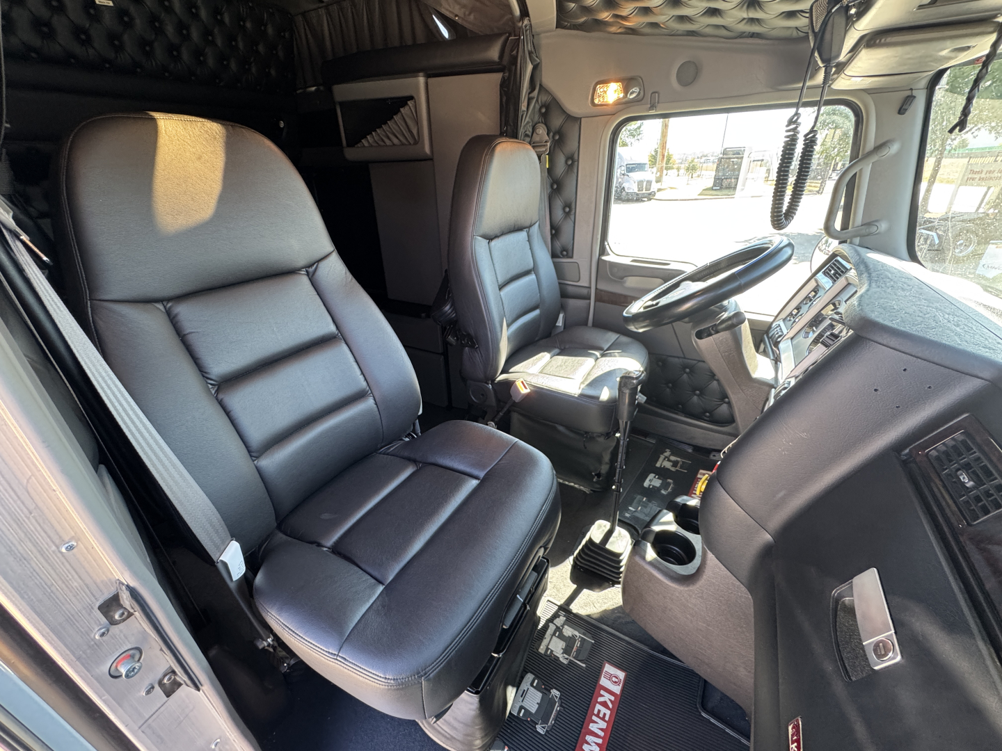 Kenworth W900L truck interior showing driver and passenger seats, dashboard, steering wheel, and center console.