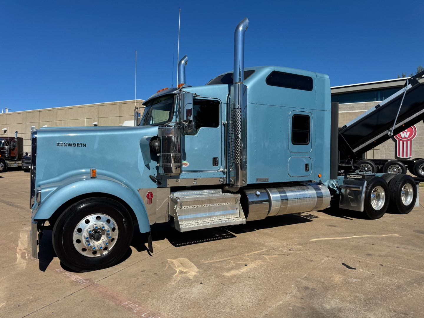 Kenworth W900L truck left side view showing sleeper cab, chrome exhaust stacks, blue paint, aluminum steps, and wheel end.