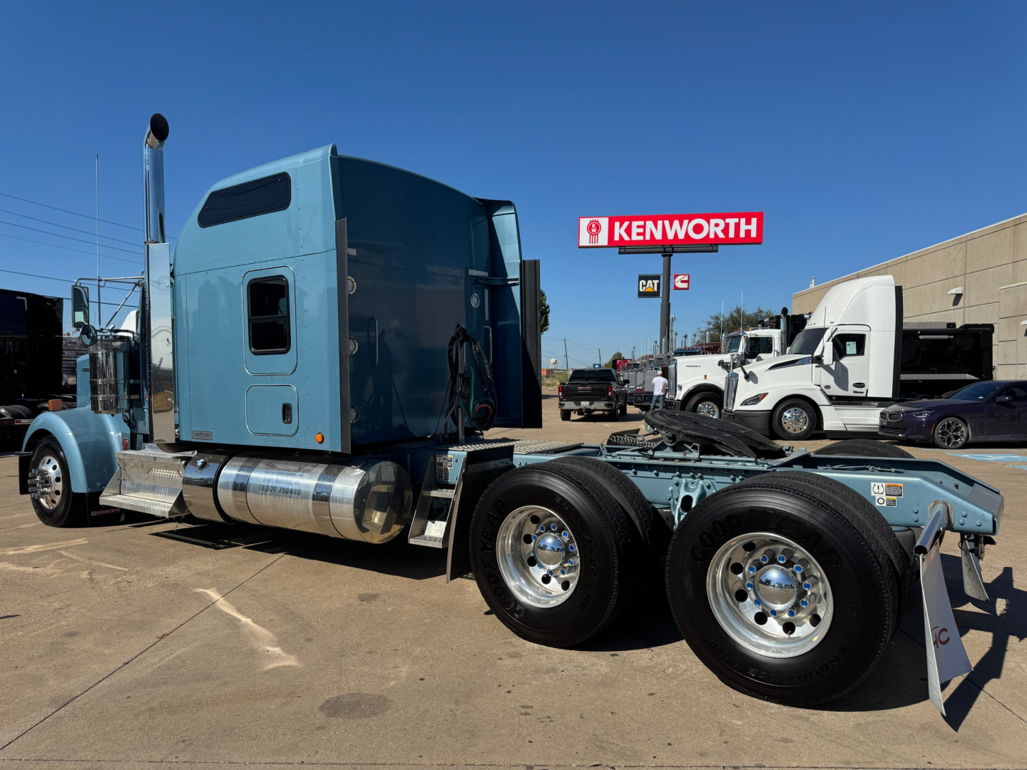 Kenworth W900L tractor cab from side view showing blue paint, twin rear axles, fuel tanks, and chrome wheels.