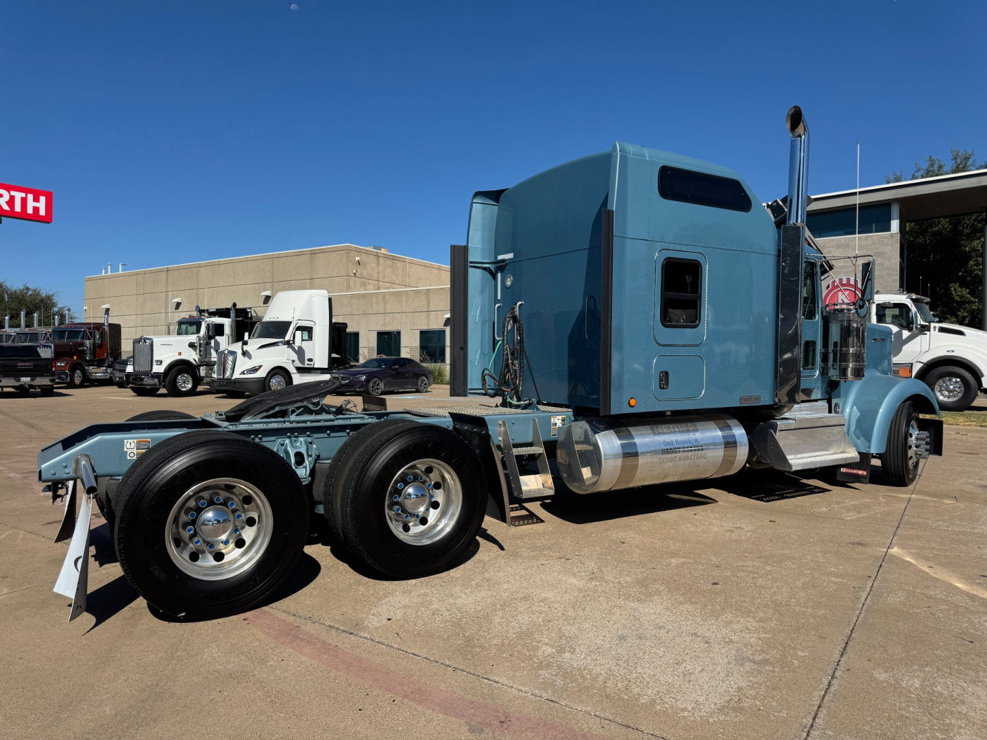 Kenworth W900L tractor in a lot showing blue cab and dual rear axles with chrome wheels and exhaust stack.
