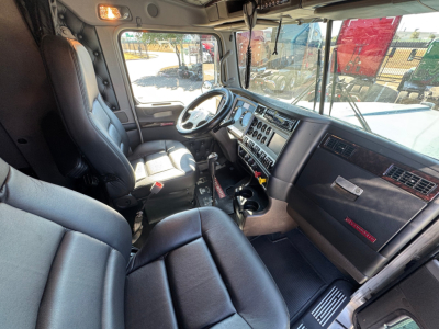 Kenworth W900L truck cabin interior showing steering wheel, dashboard with gauges, driver seat, and center console from passenger side view.