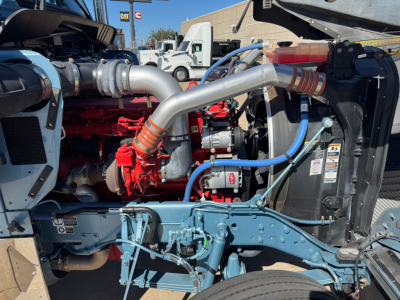Kenworth W900L engine bay with blue chassis, red turbo/intercooler piping, and silver exhaust pipe; visible radiator and hoses.