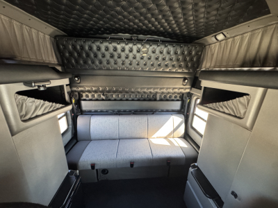 Interior cab of a 2025 Kenworth W900L sleeper showing overhead bunk area and cushioned seating with diamond-stitched panels.