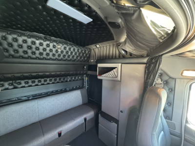 Interior of a Kenworth W900L sleeper cab showing quilted black upholstery, storage compartments, and captain seat.