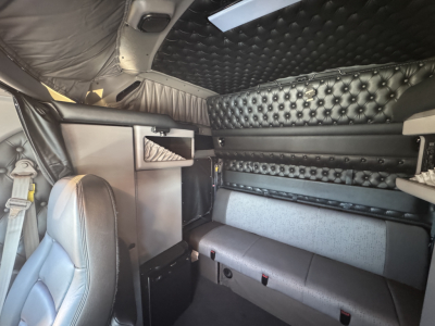 Truck cab interior showing quilted black leather-style sleeper area and seating, with storage compartments and padded walls in a Kenworth W900L.