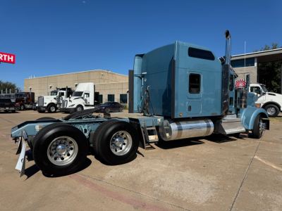 Kenworth W900L tractor in a lot showing blue cab and dual rear axles with chrome wheels and exhaust stack.