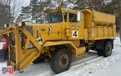 Dump truck with snow on ground showing Oshkosh P2323-6 with sander, yellow, side view, operator cab, large front plow and dump bed, number 4 tag on door.