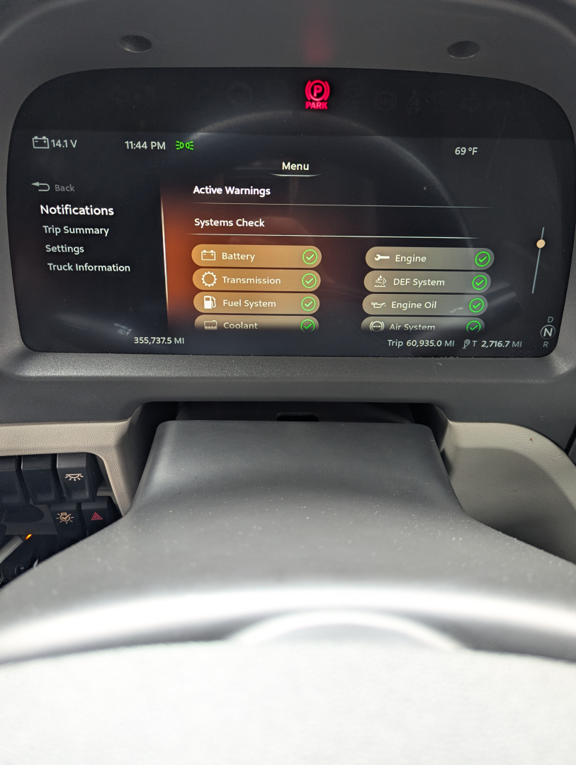 Peterbilt 579 interior dashboard display showing active warnings and system checks, with green check marks on battery, transmission, fuel system, coolant, engine, DEF, and other subsystems. 69°F outside, time 11:44 PM.
