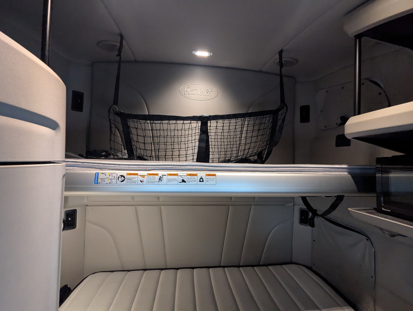 Peterbilt 579 truck sleeper cab interior showing upper bunk, storage net, and light grey padded bunk cushions.